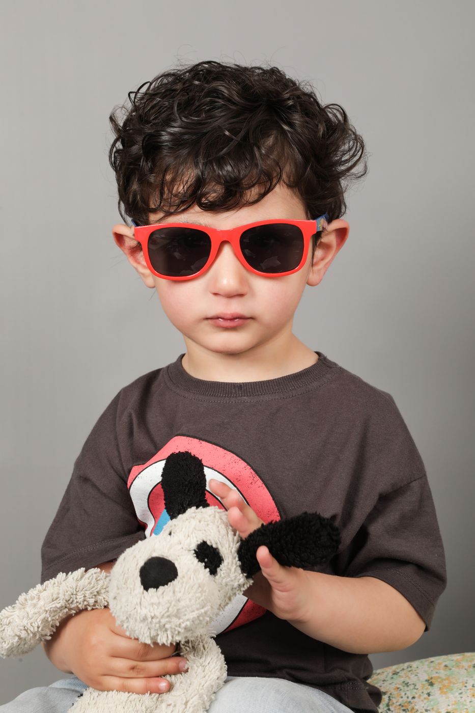 A boy in red sunglasses cuddling a well-loved toy dog