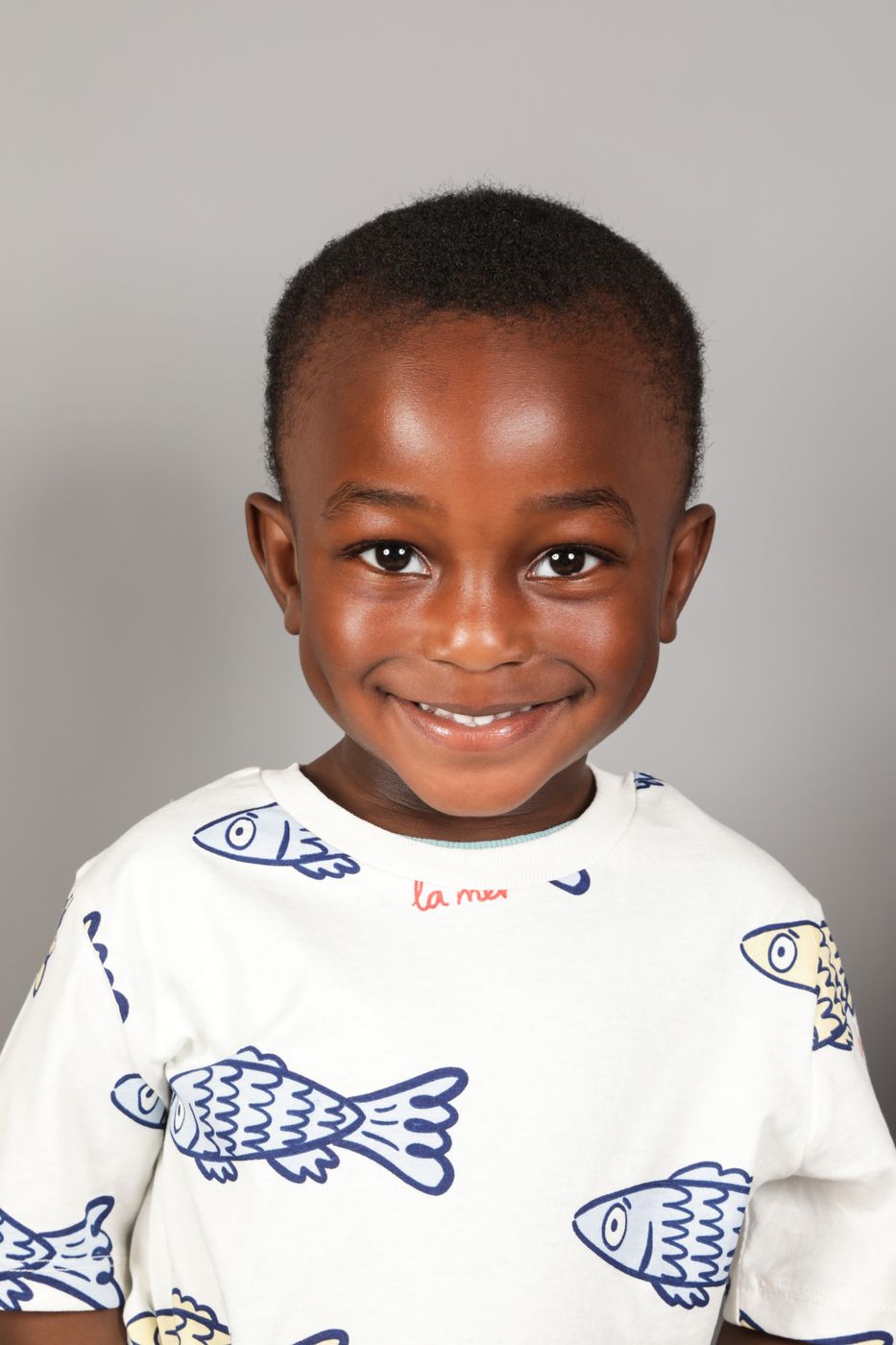 A boy in a fish-print top with a huge smile