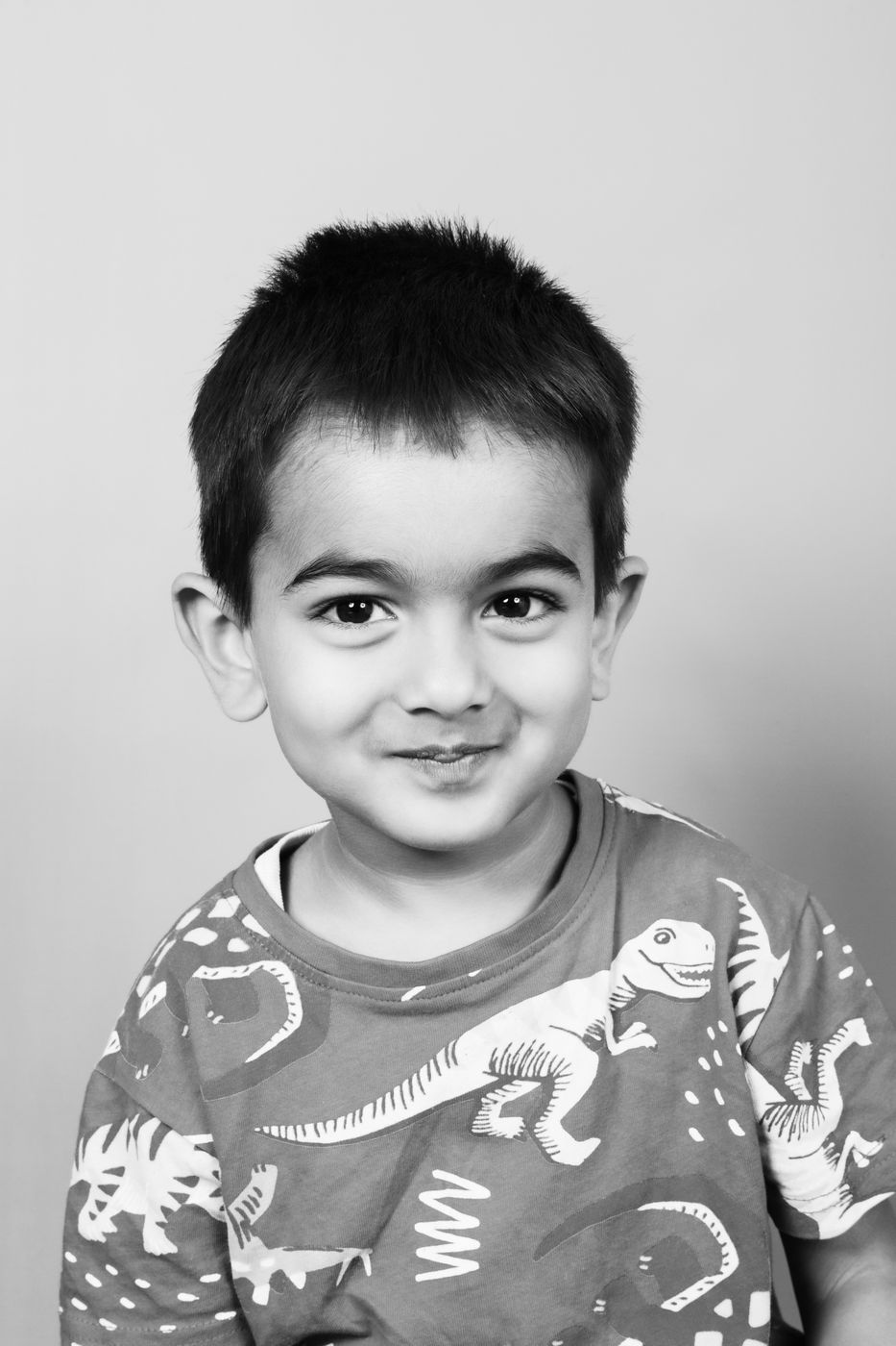 Black and white portrait of a boy in a dinosaur t-shirt, smiling shyly