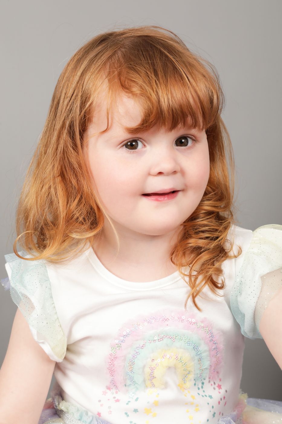A girl with long red hair and a rainbow top, smiling
