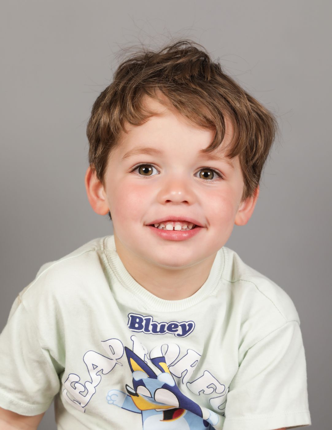 A boy with tousled brown hair grinning at the camera