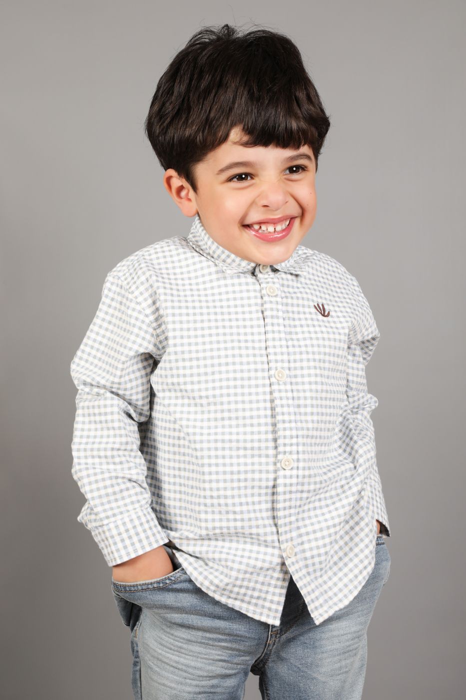 A boy in a checked shirt laughing with his hands in his pockets