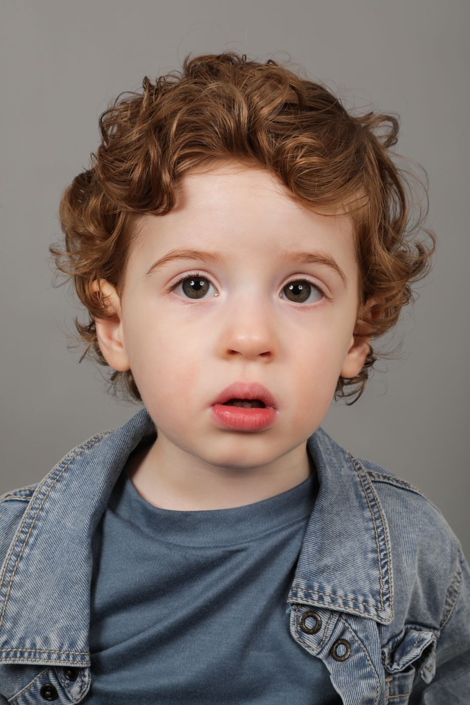 A toddler with curly auburn hair in a denim jacket