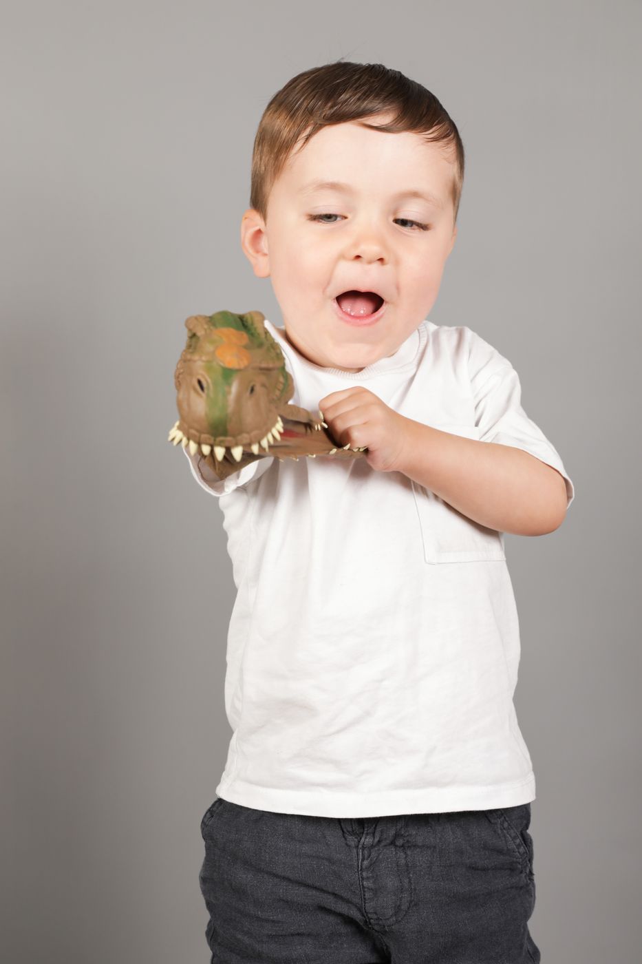 A boy in a white shirt roaring along with his toy dinosaur