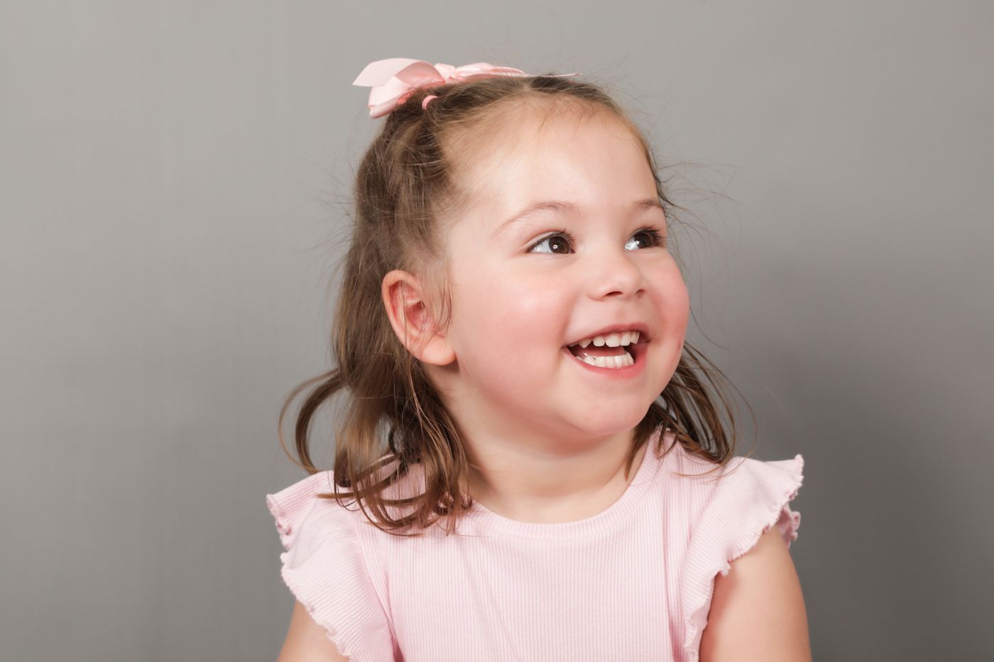 A girl with a pink bow laughing and looking off to one side