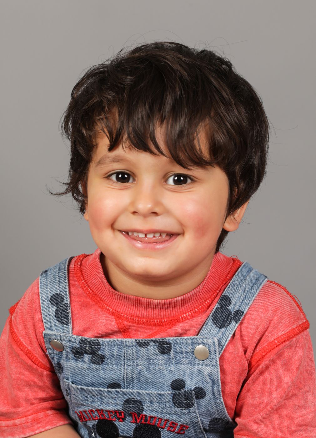 A beaming boy in red and denim dungarees